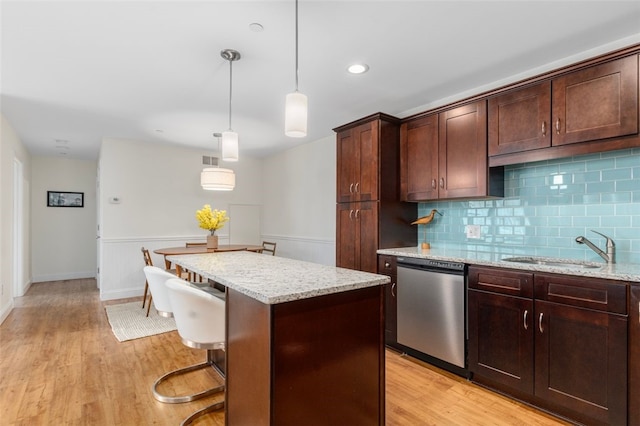 kitchen with light wood-style flooring, a kitchen island, a sink, light stone countertops, and dishwasher