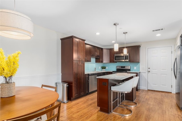 kitchen with dark brown cabinetry, visible vents, light wood-style flooring, a kitchen island, and stainless steel appliances