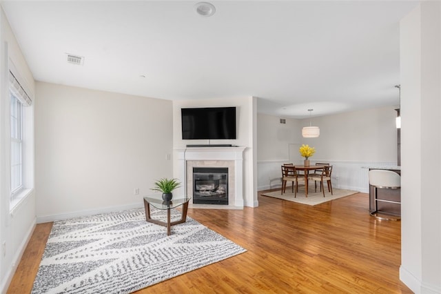 living area with light wood-style flooring, a fireplace, visible vents, and baseboards