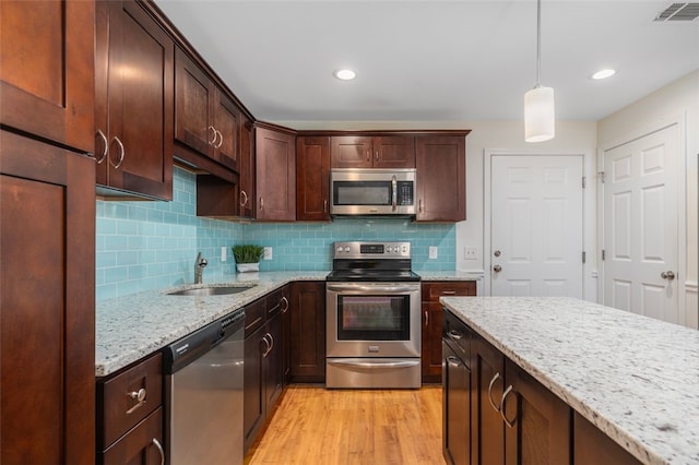 kitchen featuring visible vents, light stone countertops, light wood-type flooring, stainless steel appliances, and a sink