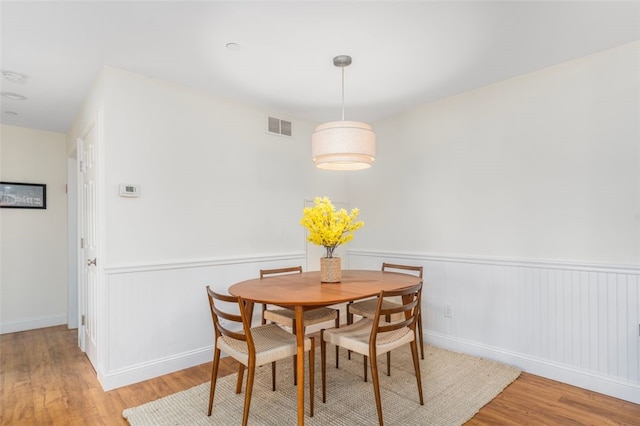 dining area featuring a wainscoted wall, visible vents, and wood finished floors