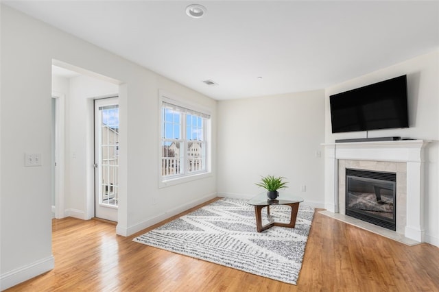 living area featuring visible vents, baseboards, wood finished floors, and a tile fireplace