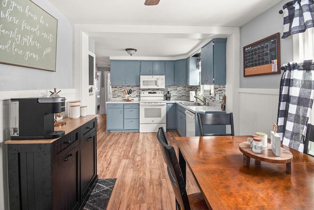 kitchen featuring blue cabinets, white appliances, a wainscoted wall, and light wood-style flooring