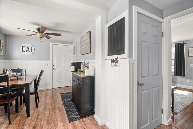 dining space featuring a wainscoted wall, ceiling fan, and light wood-style floors