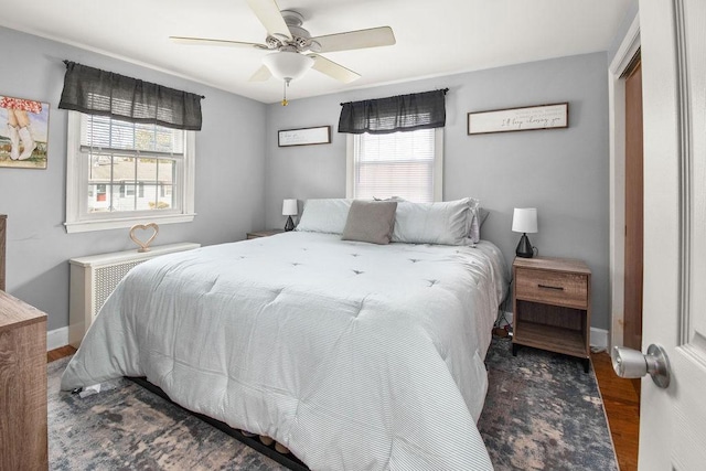 bedroom featuring a ceiling fan, radiator heating unit, baseboards, and wood finished floors