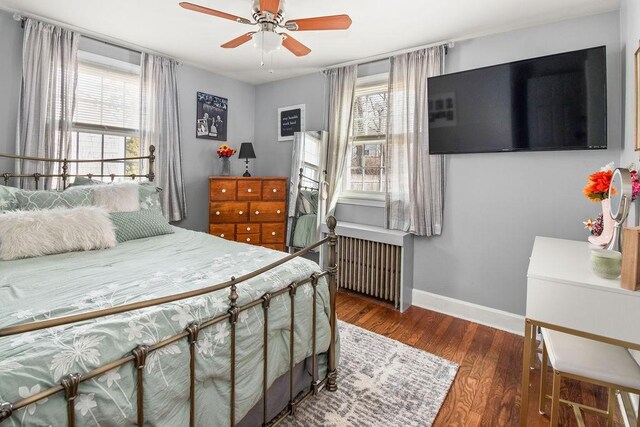 bedroom with radiator, multiple windows, wood finished floors, and baseboards