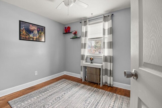 spare room with baseboards, wood finished floors, a ceiling fan, and radiator