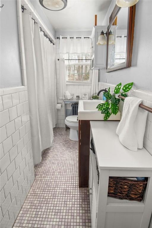 full bath with toilet, a shower with shower curtain, vanity, tile walls, and tile patterned floors