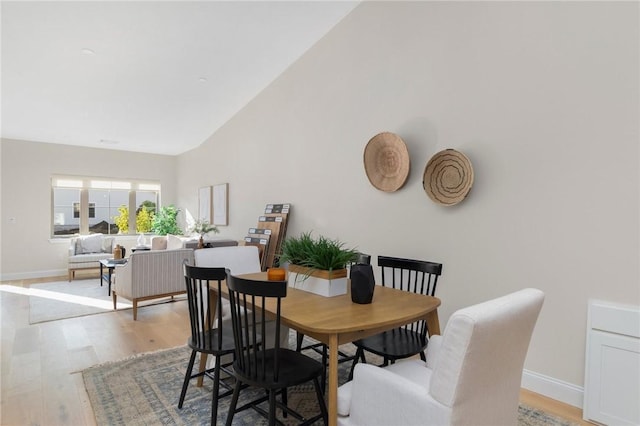 dining area featuring high vaulted ceiling, light wood finished floors, and baseboards