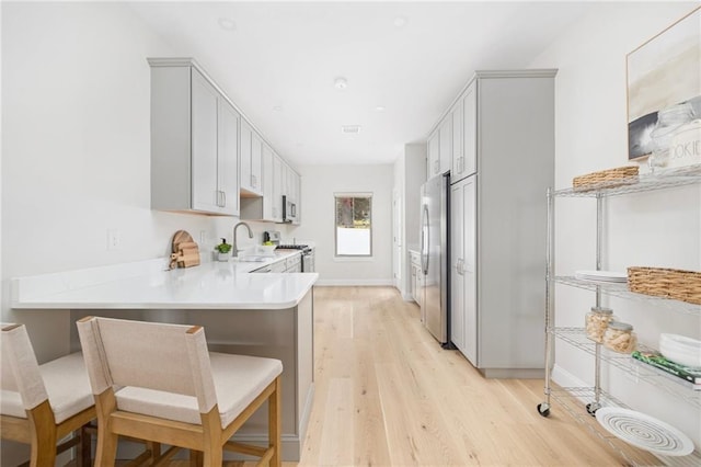 kitchen with a peninsula, a sink, light wood-style floors, light countertops, and appliances with stainless steel finishes