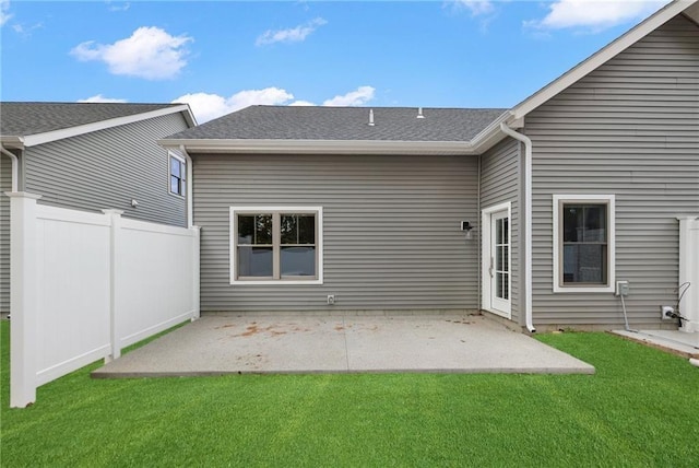 rear view of property featuring roof with shingles, fence, a lawn, and a patio