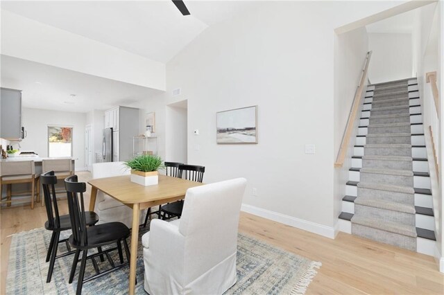 dining area with visible vents, baseboards, vaulted ceiling, stairs, and light wood-type flooring