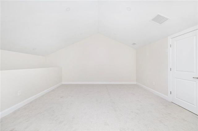 additional living space with baseboards, visible vents, vaulted ceiling, and light colored carpet