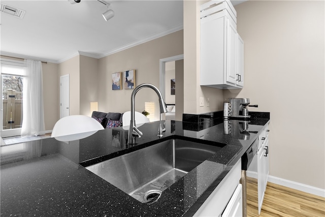 kitchen featuring a sink, visible vents, white cabinetry, ornamental molding, and light wood finished floors