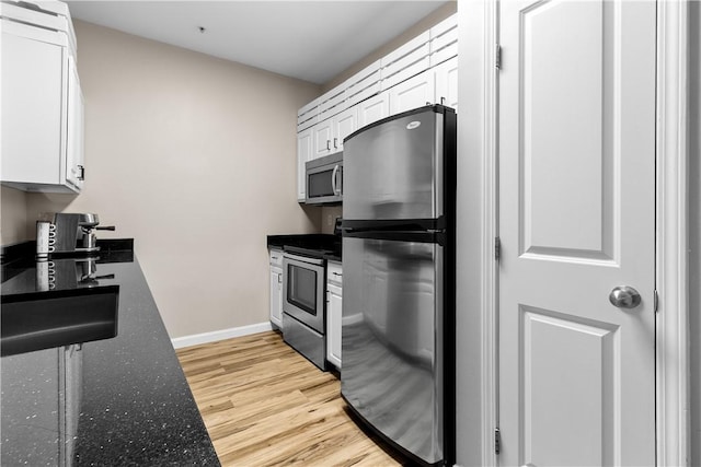 kitchen featuring light wood-style flooring, baseboards, white cabinets, appliances with stainless steel finishes, and dark stone countertops