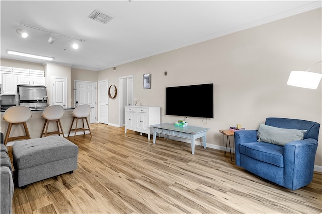 living area featuring light wood-style floors, visible vents, ornamental molding, and baseboards