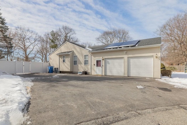 view of front of property with an attached garage, fence, driveway, a gate, and roof mounted solar panels