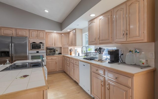 kitchen with lofted ceiling, light brown cabinets, a sink, appliances with stainless steel finishes, and tile counters