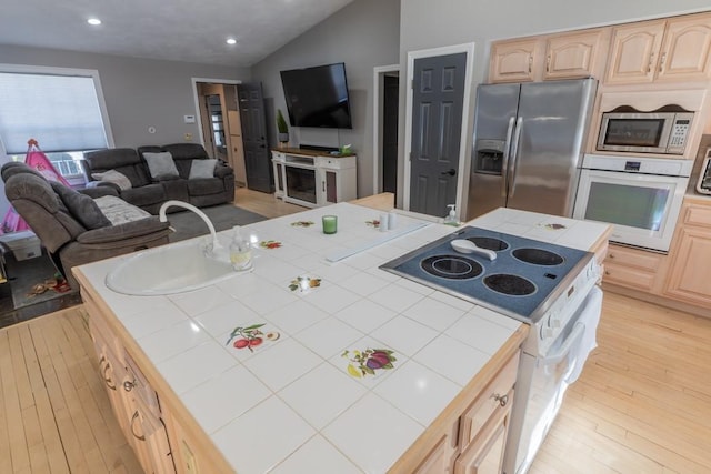 kitchen featuring tile counters, lofted ceiling, open floor plan, stainless steel appliances, and light brown cabinetry