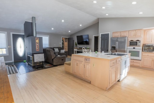 kitchen with a sink, white appliances, light brown cabinets, and light wood-style flooring