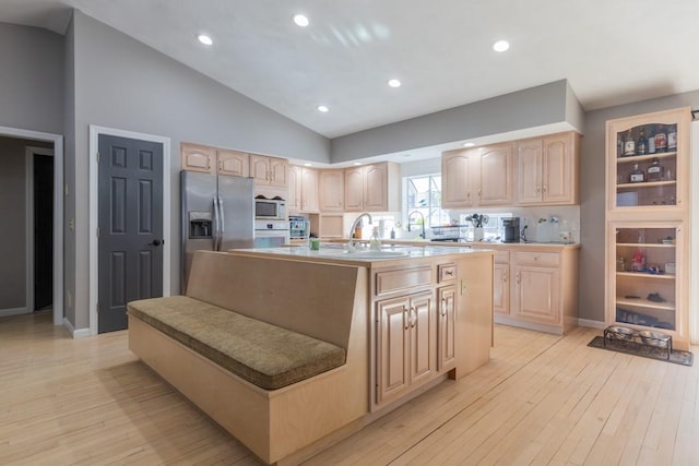 kitchen featuring lofted ceiling, white appliances, light brown cabinets, and a center island with sink