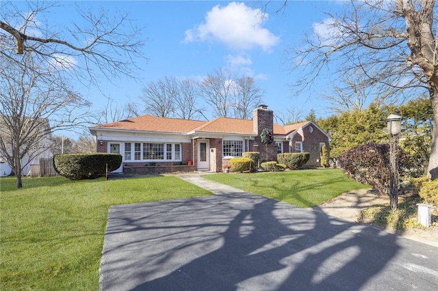 view of front of property featuring driveway, brick siding, a chimney, and a front yard