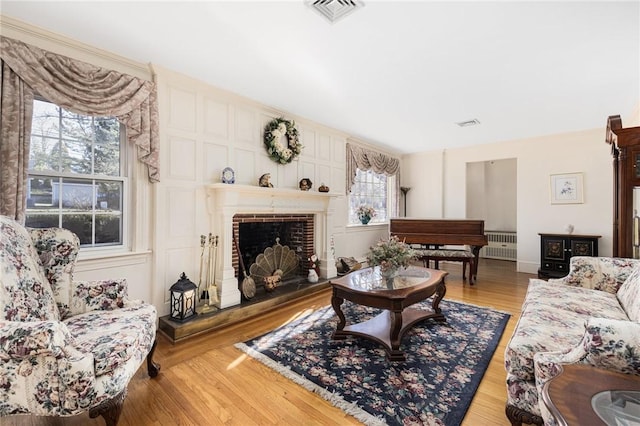 living area featuring a fireplace with raised hearth, radiator heating unit, wood finished floors, and visible vents