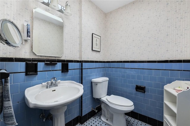 bathroom featuring a wainscoted wall and wallpapered walls