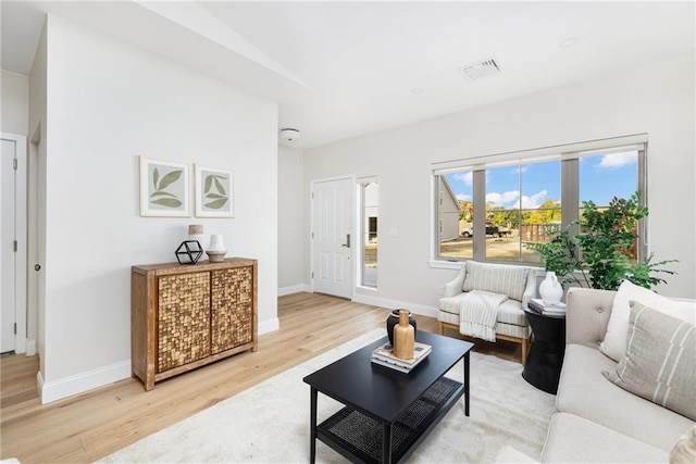 living room with light wood-type flooring, visible vents, and baseboards