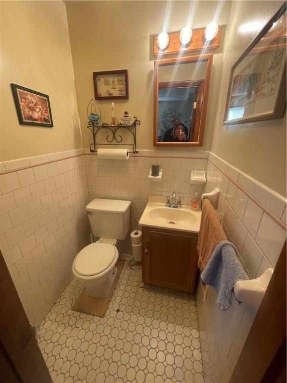 half bathroom featuring toilet, vanity, tile walls, and wainscoting