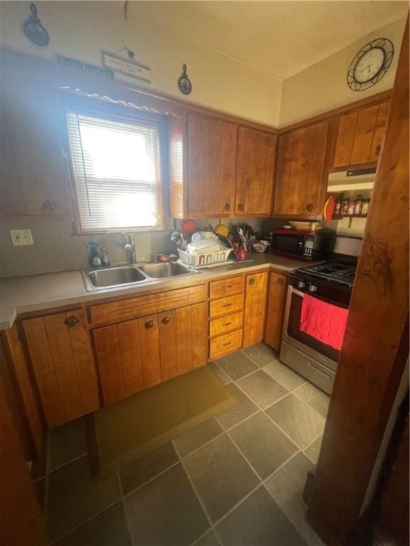 kitchen with dark tile patterned floors, gas stove, a sink, black microwave, and under cabinet range hood