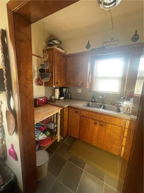 kitchen with brown cabinetry, light countertops, a sink, and dark tile patterned flooring