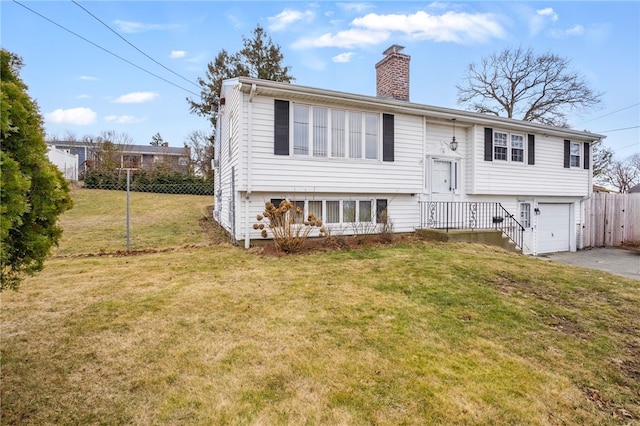 raised ranch featuring driveway, a chimney, an attached garage, fence, and a front yard