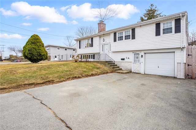 bi-level home featuring driveway, a front lawn, a chimney, and an attached garage