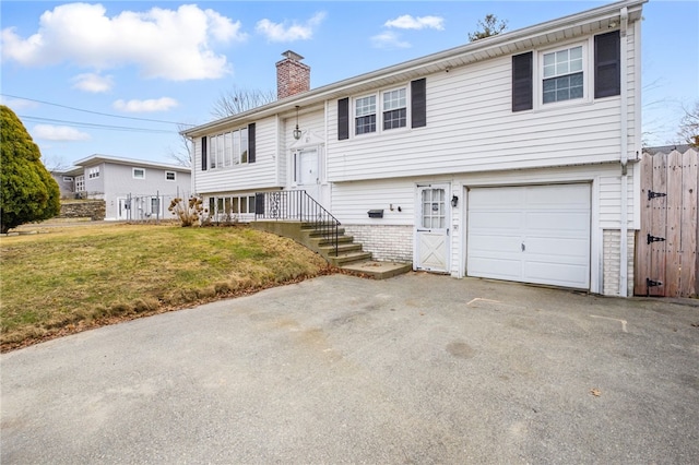 raised ranch with an attached garage, a chimney, fence, and a front lawn