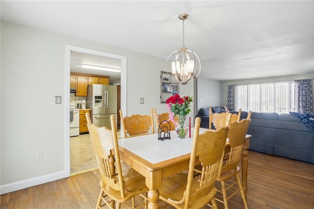 dining area with baseboards, light wood-style flooring, and a notable chandelier