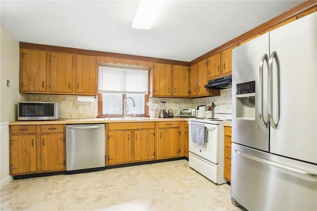 kitchen with appliances with stainless steel finishes, light countertops, a sink, and under cabinet range hood