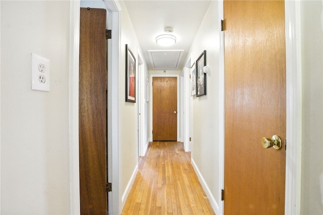 hallway with light wood finished floors, attic access, and baseboards