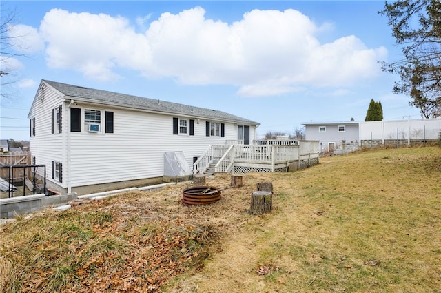 back of property featuring a deck, fence, a fire pit, and a lawn