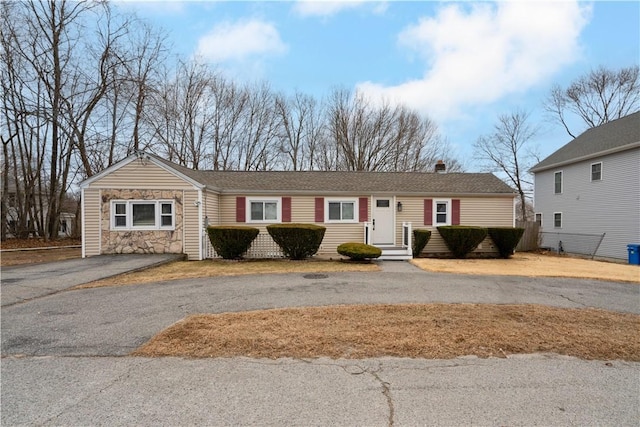 single story home featuring stone siding, driveway, and a chimney