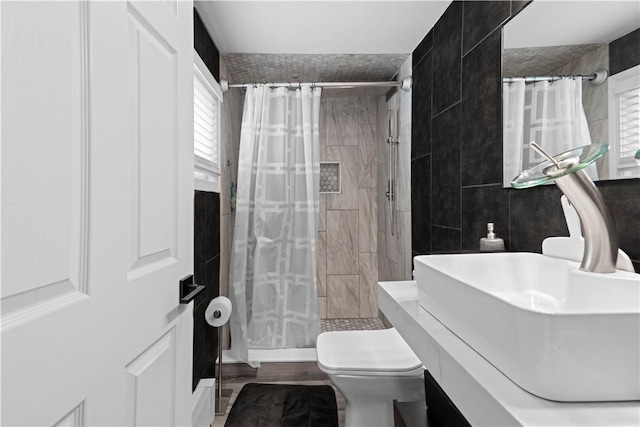 full bath with toilet, a wealth of natural light, a sink, and tiled shower