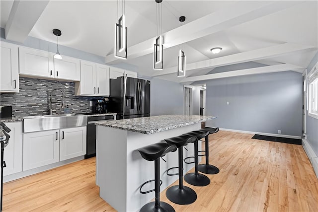 kitchen featuring black fridge with ice dispenser, decorative backsplash, a sink, beamed ceiling, and a kitchen bar