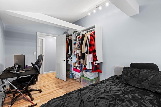 bedroom featuring rail lighting, a closet, vaulted ceiling, and wood finished floors