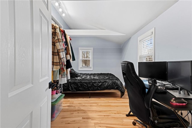 bedroom with track lighting, vaulted ceiling, and wood finished floors