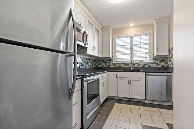 kitchen with tile patterned flooring, a sink, appliances with stainless steel finishes, backsplash, and dark countertops