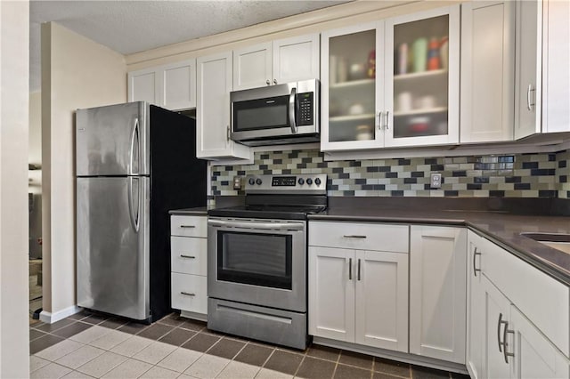 kitchen featuring dark countertops, white cabinetry, stainless steel appliances, and decorative backsplash