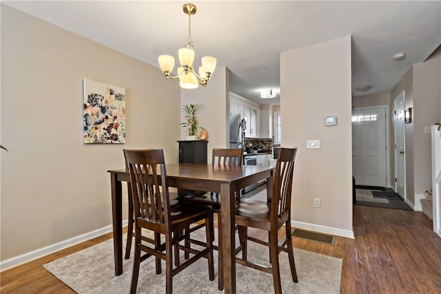 dining room featuring visible vents, baseboards, a chandelier, and wood finished floors