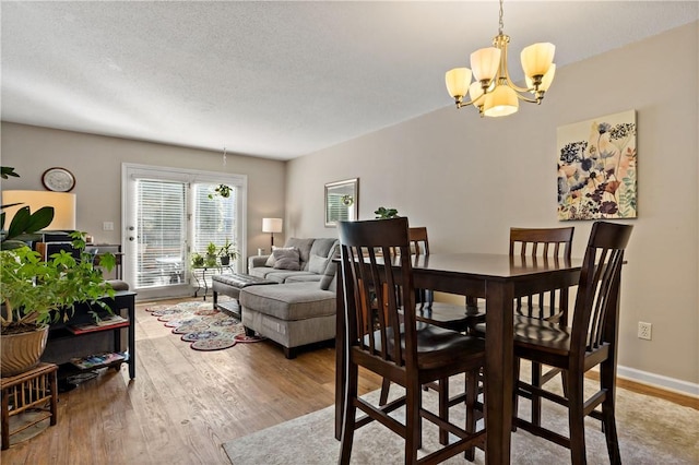 dining space featuring a notable chandelier, a textured ceiling, baseboards, and wood finished floors