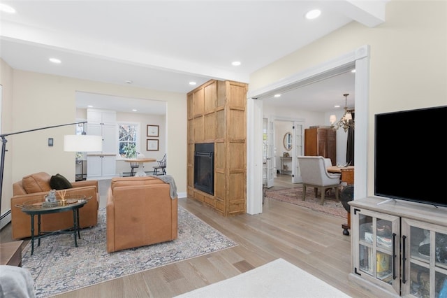 living room featuring a notable chandelier, light wood-type flooring, a fireplace, and recessed lighting