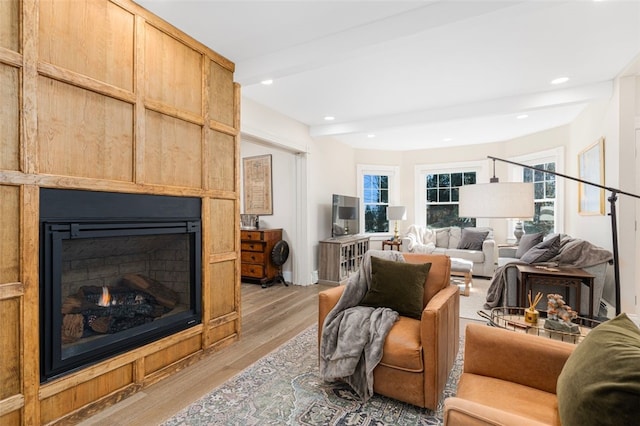 living room with a warm lit fireplace, light wood finished floors, and recessed lighting